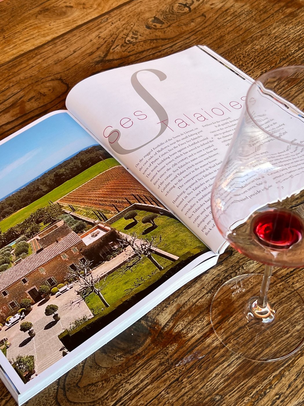 Glass of red wine beside a magazine feature on the Ses Talaioles vineyard in Mallorca